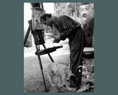 Photo de Charles Féola peignant une toile sur un chevalet en compagnie de son chien